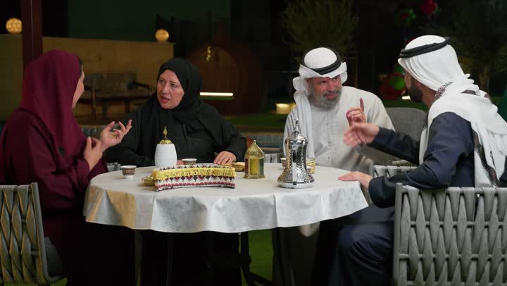 فطور رمضاني عائلي في مطعم مزين بديكورات رمضانية, اسلاميات وعبادة,عائلة عربية خليجية إماراتية تجلس على سفرة الطعام تقوم بالتحدث والتسامر في اجواء شهر رمضان الكريم, أسرة اماراتيه مستمتعه بالجلوس في الخارج، ولد اماراتي مبتسم يحمل فانوس معدني مزخرف ولون