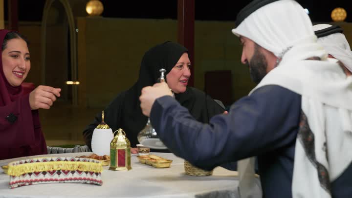 الاستمتاع بالمشروبات الساخنة في المجالس العربية، كرم الضيافة وحسن الاستقبال، العادات والتقاليد في الامارات العربية المتحدة،رجل عربي خليجي اماراتي يرتدي الكندوره يحمل بيده دله قهوه ويقوم بتقديمها الي عائلته