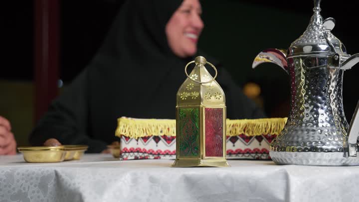دله قهوه وفانوس معدني ملون علي طاوله الافطار، كرم الضيافة وحسن الاستقبال، العادات والتقاليد في الامارات العربية المتحدة، امرأه مسنه عربيه خليجيه اماراتيه ترتدي العباءه السوداء برفقه زوجها وعائلتها، سيده مسنه سعوديه تتحدث في موضوع ما