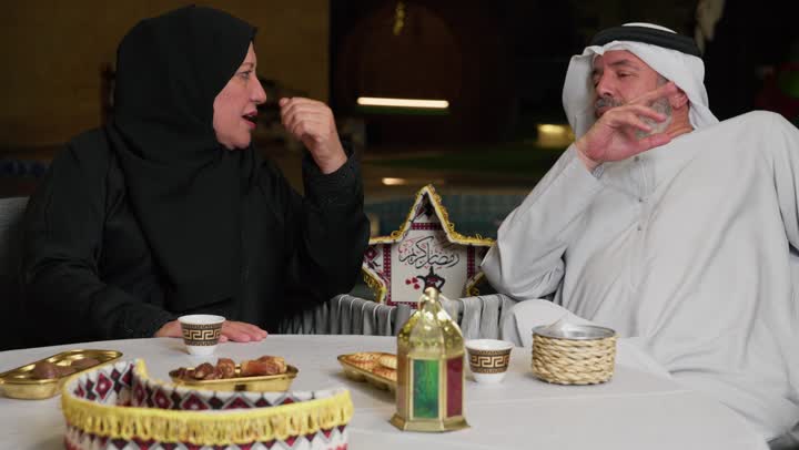 زيارات وتجمعات عائليه، كرم الضيافة وحسن الاستقبال، العادات والتقاليد في الامارات العربية المتحدة، رجل مسن عربي خليجي اماراتي يرتدي الكندوره برفقه زوجته وعائلته، ديكورات وزينه رمضان المبارك علي الطاوله
