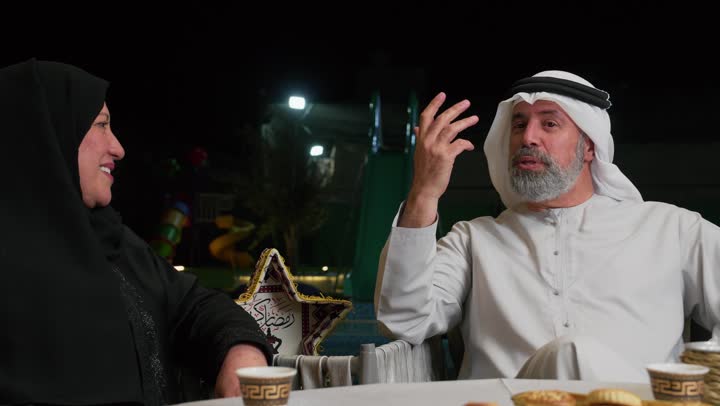 تبادل الأحاديث بين أفراد الأسرة، أجواء عائلية دينية رمضانية سعيدة، فوانيس معدنية مزخرفة ملونة على سفرة الطعام، زينة المناسبات الإسلامية، أداء فريضة الصيام في شهر رمضان المبارك، عائلة عربية خليجية اماراتيه مجتمعة حول مائدة الطعام
