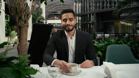 تأثير الكافيين على نشاط الدماغ والذاكرة، التلذذ باحتساء مشروبات الكافيهات الجاهزة، كافيه راقي في الإمارات العربية المتحدة، الاستمتاع بالاجواء الهادئة خارج المنزل، رجل عربي خليجي اماراتي يرتدي البدلة الرسمية يجلس في المقهى يقوم بشرب القهوة