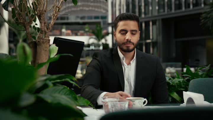 التلذذ باحتساء مشروبات الكافيهات الجاهزة، كافيه راقي في الإمارات العربية المتحدة، تأثير الكافيين على نشاط الدماغ والذاكرة، الاستمتاع بالاجواء الهادئة خارج المنزل، تصوير مقرب لرجل عربي خليجي اماراتي يرتدي البدلة الرسمية يجلس في المقهى يقوم بشرب القهوة