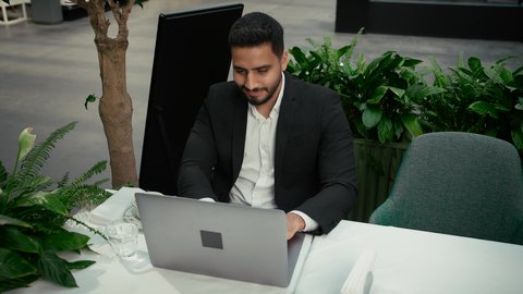 التلذذ والاستمتاع باحتساء القهوة، تصوير مقرب لرجل عربي خليجي إماراتي يرتدي الزي الرسمي يجلس في المقهى ويقوم بإنجاز العمل عن بعد عبر جهاز الحاسوب، جلسة خارجية هادئة في كافيه راقي في الإمارات، استخدام جهاز تقني حديث ومتطور