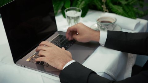 امتلاك مهارة الكتابة بسرعة، عرض شاشة لابتوب سوداء فارغة، الاستمتاع باحتساء القهوة، تصوير مقرب لأيدي رجل عربي خليجي إماراتي يجلس في المقهى ويقوم بالضغط على أزار لوحة المفاتيح، إنجاز العمل عن بعد عبر جهاز الحاسوب، كافيه راقي في الإمارات العربية المتحدة