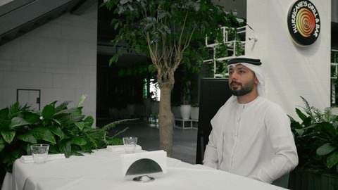 مفهوم الاستقبال والترحيب، إيماءات السعادة والسرور برؤية الأصدقاء، إلقاء التحيه والسلام, صداقة وتعارف وبناء علاقات اجتماعية، رجل عربي خليجي إماراتي يرتدي الكندورة والغترة يقابل صديقه في المقهى ويقوم بمصافحته، كافيه راقي في الإمارات العربية المتحدة