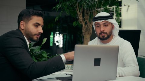 التوقيع على صفقات ومشاريع جديدة، انجاز المهام عن بعد عبر الحاسوب المحمول في الكافيه، الاستمتاع بشرب القهوة في المقهى، المناقشة بين الزملاء لإدارة الأعمال وتنظيمها، تصوير مقرب لرجل عربي خليجي اماراتي يرتدي البدلة الرسمية في اجتماع عمل مع عميل يرتدي الزي التقليدي.