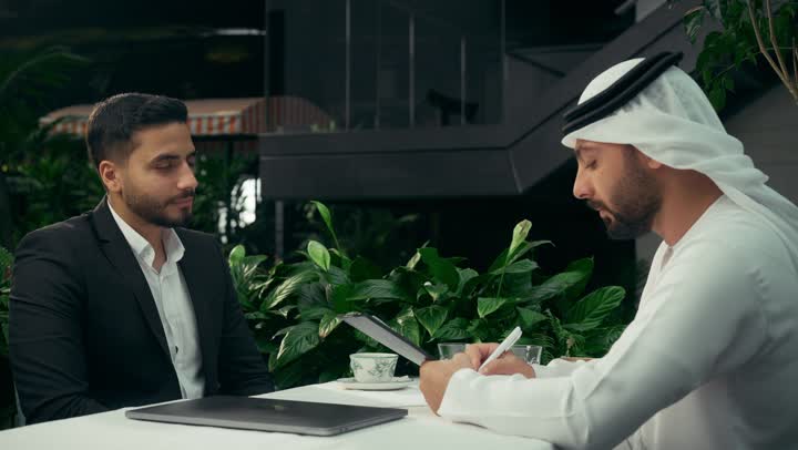 إيماءات السرور والسعادة، بناء شراكات واتفاقيات وصفقات جديدة، التحقق والتدقيق في شروط العقد، تصوير مقرب رجل أعمال عربي خليجي إماراتي يرتدي الزي التقليدي يصافح رجل أعمال يرتدي البدلة الرسمية، الإتفاق على المشاريع التجارية، التوقيع على أوراق إحدى العقود