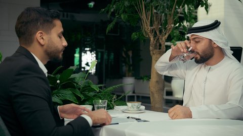 إيماءات الرفض وعدم الموافقة، قراءة البنود الخاصة بالعمل، الحوار والنقاش بين الزملاء لإدارة الأعمال، بناء شراكات واتفاقيات جديدة، تصوير مقرب لزميلين عربيين خليجيين إماراتيين يجلسان في المقهى يقومان بقراءة أوراق العقود والتقارير، التحقق والتدقيق في شروط العقد