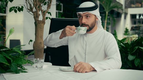 كافيه راقي في الإمارات العربية المتحدة، تأثير الكافيين على نشاط الدماغ والذاكرة، الاستمتاع بالاجواء الهادئة خارج المنزل، رجل عربي خليجي اماراتي يرتدي الكندورة والغترة يجلس في المقهى يقوم بشرب القهوة