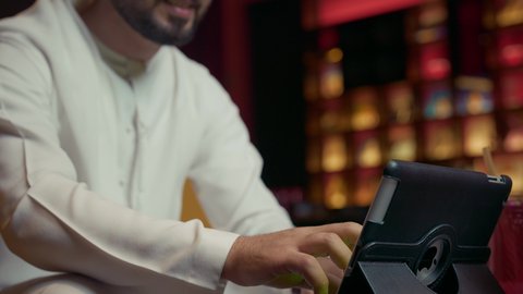 فوز الفريق المفضل، رفع إصبع الإبهام بإيماءات السعادة والسرور، تصوير مقرب لرجل عربي خليجي إماراتي يرتدي الكندورة والغترة يجلس في المقهى ويقوم بإنجاز العمل عن بعد عبر التابلت، كافيه راقي في الإمارات العربية، تصفح مواقع التواصل الاجتماعي باستخدام الجهاز اللوحي