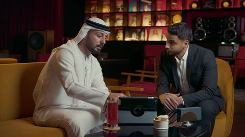الحوار والنقاش بين الزملاء لإدارة الأعمال وتنظيمها، استخدام التقنيات الحديثة والمطورة، انجاز المشاريع والمهام عن بعد في الكافيه، رجل عربي خليجي اماراتي في اجتماع عمل مع عميل جديد يرتدي البدلة الرسمية، استخدام جهاز التابلت المحمول بإيماءات الاندماج والتركيز