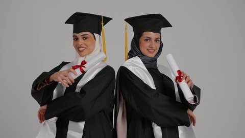 أهمية الدراسة الجامعية والفرح بتحقيق النجاح، التعليم الجامعي الاماراتي، الاحتفال بالتخرج من الجامعة بإيماءات السعادة والفرح، تصوير مقرب لخريجتين عربيتين خليجيتين اماراتيتين مبتسمتين يرتديان ملابس التخرج وتمسكان وثيقة التفوق