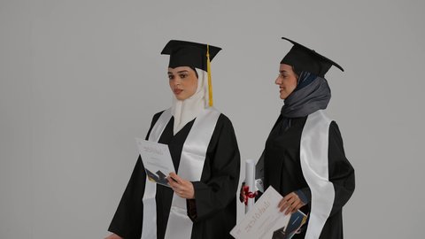 التعليم الجامعي الاماراتي، إيماءات السعادة والفرح، المناسبات والاحتفالات الجامعية, أهمية الدراسة الجامعية والفرح بتحقيق النجاح، الشعور بالفخر والثقه بالنفس ، الاحتفال بالتخرج من الجامعة ، تصوير مقرب لخريجتين عربيتين خليجيتين اماراتيتين مبتسمتين يرتديان ملابس التخرج وتمسكان وثيقه النجاح