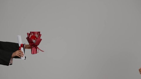 الاحتفال بالتخرج من الجامعة، تحقيق حلم النجاح, الشعور بالفخر والثقه بالنفس ،مفهوم الاجتهاد والتفوق ، إيماءات الفرح والسرور، إنهاء الدراسة الجامعية، تصوير مقرب من الخلف لطالبة عربية خليجية اماراتيه محجبة ترتدي روب التخرج ، تستلم وثيقه النجاح والورد .