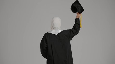 مفهوم الاجتهاد والتفوق ، إيماءات الفرح والسرور، الاحتفال بالتخرج من الجامعة، الشعور بالفخر والثقه بالنفس ، تحقيق حلم النجاح, إنهاء الدراسة الجامعية، تصوير مقرب من الخلف لطالبة عربية خليجية اماراتيه محجبة ترتدي روب التخرج ، ترفع قبعه التخرج بايديها