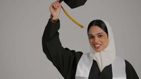 Gestures of joy and happiness, celebrating university graduation, feeling proud and self-confident, achieving the dream of success, completing university studies, the concept of diligence and excellence, a close-up of a veiled Emirati Gulf Arab student wearing a graduation robe, raising the success document and graduation cap in her hands