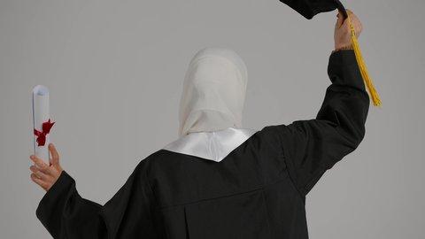 الاحتفال بالتخرج من الجامعة، الشعور بالفخر والثقه بالنفس ، تحقيق حلم النجاح, إنهاء الدراسة الجامعية، مفهوم الاجتهاد والتفوق ، إيماءات الفرح والسرور، تصوير مقرب من الخلف لطالبة عربية خليجية اماراتيه محجبة ترتدي روب التخرج ، ترفع وثيقه النجاح وقبعه التخرج بايديها