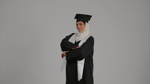 Gestures of joy and happiness, finishing university studies, feeling proud and self-confident, achieving the dream of success, celebrating university graduation, the concept of diligence and excellence, a close-up of a veiled Emirati Gulf Arab student wearing a graduation robe and cap, standing with crossed hands