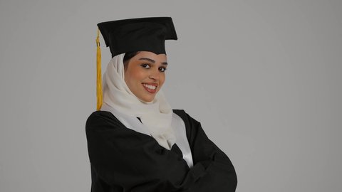 الاحتفال بإنهاء الدراسة الجامعية، الشعور بالفخر والثقه بالنفس ، تحقيق حلم النجاح, الاحتفال بالتخرج من الجامعة، مفهوم الاجتهاد والتفوق ، تصوير مقرب لطالبة عربية خليجية اماراتيه محجبة ترتدي روب التخرج والقبعة تقف بايدي متقاطعه