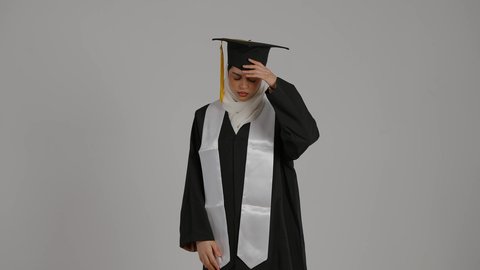 الشعور بالتعب والإرهاق, الإصابة بنوبات الشقيقة ، إنهاء الدراسة الجامعية، تحقيق حلم النجاح, الاحتفال بالتخرج من الجامعة، مفهوم الاجتهاد والتفوق ، تصوير مقرب لطالبة عربية خليجية اماراتيه محجبة ترتدي روب التخرج والقبعة تضع يدها على رأسها بإيماءات الدوار و الألم