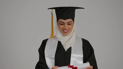 Achieving the dream of success, celebrating university graduation, the concept of hard work and excellence, raising the success certificate with expressions of pride, feeling self-confidence, completing university studies, a close-up of a veiled Emirati Gulf Arab student wearing a graduation robe, raising the success certificate with gestures of pleasure