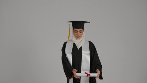 الاحتفال بالتخرج من الجامعة، مفهوم الاجتهاد والتفوق، الاشاره الى وثيقه النجاح بتعابير الفخر ، تحقيق حلم النجاح, الشعور بالثقة بالنفس ،إنهاء الدراسة الجامعية، تصوير مقرب لطالبة عربية خليجية اماراتيه محجبة ترتدي روب التخرج ، ترفع وثيقه النجاح بايماءات السرور