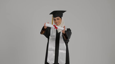 Celebrating the completion of university studies, the concept of diligence and excellence, the feeling of self-confidence and pride, the joy of achieving success, a close-up of a veiled Emirati Gulf Arab student wearing a graduation robe, raising the success document with gestures of pleasure