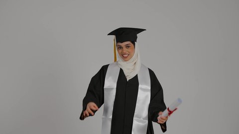 ايماءات الجودة والامتياز ،الاحتفالات والمناسبات الجامعية, تعابير السرور و الفرح لتحقيق النجاح، الشعور بالثقة بالنفس والفخر، جودة التعليم في المملكة ، مفهوم الاجتهاد والتفوق، تصوير مقرب لطالبة عربية خليجية اماراتيه محجبة ترتدي روب التخرج ، ترفع وثيقه النجاح بايماءات السعاده