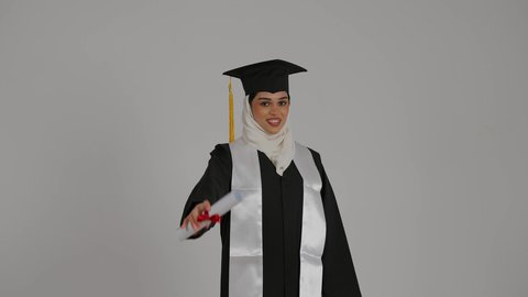 الاحتفالات والمناسبات الجامعية, تعابير السرور و الفرح لتحقيق النجاح، الشعور بالثقة بالنفس والفخر، جودة التعليم في المملكة ، مفهوم الاجتهاد والتفوق، تصوير مقرب لطالبة عربية خليجية اماراتيه محجبة ترتدي روب التخرج ، ترفع وثيقه النجاح بايماءات السعاده