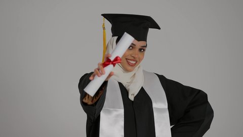 تعابير السرور و الفرح لتحقيق النجاح، الشعور بالثقة بالنفس والفخر، جودة التعليم في المملكة ، الاحتفالات والمناسبات الجامعية, مفهوم الاجتهاد والتفوق، تصوير مقرب لطالبة عربية خليجية اماراتيه محجبة ترتدي روب التخرج ، ترفع وثيقه النجاح بايماءات السعاده