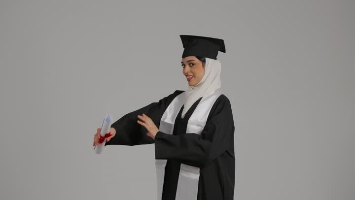 جودة التعليم في المملكة ، الاحتفالات والمناسبات الجامعية, دمج التقنيات الحديثه فى الحياه اليوميه ، تحقيق حلم النجاح ، الشعور بالثقة بالنفس والفخر، مفهوم الاجتهاد والتفوق،تصوير مقرب لطالبة عربية خليجية اماراتيه محجبة ترتدي روب التخرج ، تقف بايدي متقاطعه