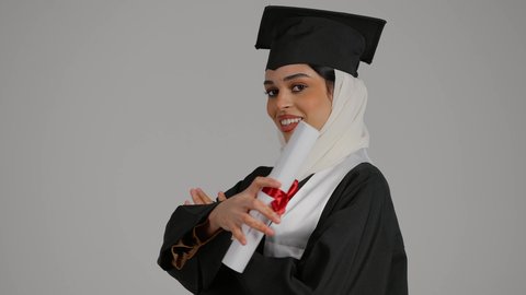 الاحتفالات والمناسبات الجامعية, دمج التقنيات الحديثه فى الحياه اليوميه ، تحقيق حلم النجاح ، الشعور بالثقة بالنفس والفخر، جودة التعليم في المملكة ، مفهوم الاجتهاد والتفوق،تصوير مقرب لطالبة عربية خليجية اماراتيه محجبة ترتدي روب التخرج ، تقف بايدي متقاطعه