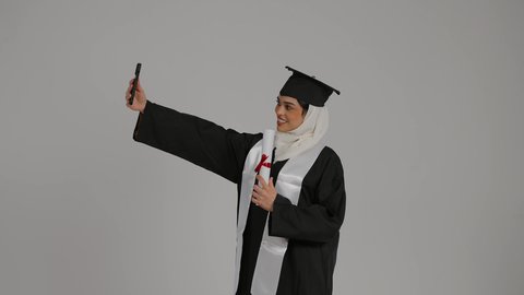 توثيق اللحظات التذكاريه ، الاحتفالات والمناسبات الجامعية, تحقيق حلم النجاح ، الشعور بالثقة بالنفس والفخر، جودة التعليم في المملكة ، مفهوم الاجتهاد والتفوق،تصوير مقرب لطالبة عربية خليجية اماراتيه محجبة ترتدي روب التخرج ، تحمل بيدها وثيقه النجاح وقبعة التخرج