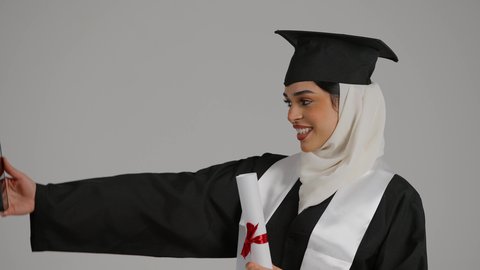 التقاط صور السيلفي ، الاحتفالات والمناسبات الجامعية, تحقيق حلم النجاح ، الشعور بالثقة بالنفس والفخر، جودة التعليم في المملكة ، مفهوم الاجتهاد والتفوق،تصوير مقرب لطالبة عربية خليجية اماراتيه محجبة ترتدي روب التخرج ، تحمل بيدها وثيقه النجاح وقبعة التخرج