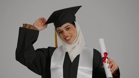 الشعور بالثقة بالنفس والفخر، جودة التعليم في المملكة ، إنهاء الدراسة الجامعية ، تحقيق حلم النجاح ، الاحتفالات والمناسبات الجامعية, مفهوم الاجتهاد والتفوق،تصوير مقرب لطالبة عربية خليجية اماراتيه محجبة ترتدي روب التخرج ، تحمل بيدها وثيقه النجاح وقبعة التخرج