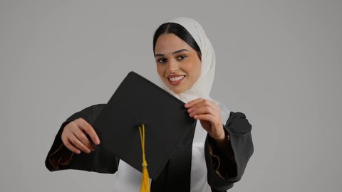 مفهوم الاجتهاد والتفوق، إنهاء الدراسة الجامعية ، تحقيق حلم النجاح ، جودة التعليم في المملكة ، الاحتفالات والمناسبات الجامعية, الشعور بالثقة بالنفس والفخر، تصوير مقرب لطالبة عربية خليجية اماراتيه محجبة ترتدي روب التخرج ، تحمل بيدها قبعه التخرج ، تضع وشاح علم الامارات على كتفها
