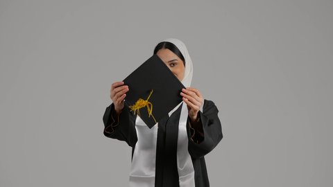 إنهاء الدراسة الجامعية ، تحقيق حلم النجاح ، الاهتمام بالاناقه والمظهر الخارجى ، جودة التعليم في المملكة ، الاحتفالات والمناسبات الجامعية, مفهوم الاجتهاد والتفوق، الشعور بالثقة بالنفس والفخر، تصوير مقرب لطالبة عربية خليجية اماراتيه محجبة ترتدي روب التخرج ، تحمل بيدها قبعه التخرج ، تضع وشاح علم الامارات على كتفها