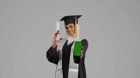 جودة التعليم في المملكة ، دمج التقنيات فى الحياه اليوميه ، الاحتفالات والمناسبات الجامعية, مفهوم الاجتهاد والتفوق، الشعور بالثقة بالنفس والفخر، تصوير مقرب لطالبة عربية خليجية اماراتيه محجبة ترتدي روب وقبعة التخرج ،تحمل بيدها الهاتف المحمول ووثيقه النجاح، تضع وشاح علم الامارات على كتفها، إنهاء الدراسة الجامعية