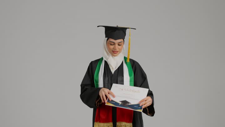 University celebrations and events, the concept of diligence and excellence, feeling self-confidence, displaying the graduation certificate with proud gestures, a close-up of a veiled Emirati Gulf Arab student wearing an abaya and graduation cap, placing the UAE flag scarf on her shoulder, holding a success document in her hand, completing university studies, quality of education in the Kingdom