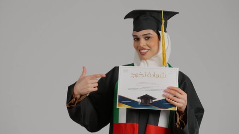 الشعور بالثقة بالنفس، الاشاره الى شهادة التخرج بايماءات الفخر ، تصوير مقرب لطالبة عربية خليجية اماراتيه محجبة ترتدي عباءه وقبعة التخرج ، تضع وشاح علم الامارات على كتفها، تحمل بيدها وثيقه النجاح، الاحتفالات والمناسبات الجامعية, مفهوم الاجتهاد والتفوق، إنهاء الدراسة الجامعية، جودة التعليم في المملكة