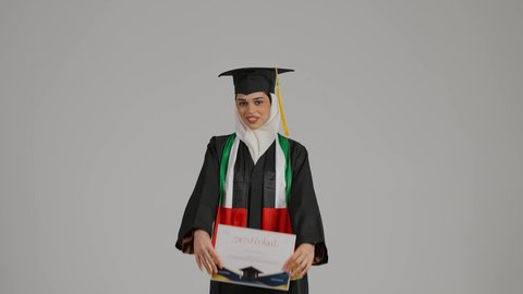 النظر الى الكاميرا بايماءات السرور ، تصوير مقرب لطالبة عربية خليجية اماراتيه محجبة ترتدي عباءه وقبعة التخرج ، تضع وشاح علم الامارات على كتفها، تحمل بيدها وثيقه النجاح، الاحتفالات والمناسبات الجامعية, مفهوم الاجتهاد والتفوق، إنهاء الدراسة الجامعية، الشعور بالفخر والثقة بالنفس، جودة التعليم في المملكة