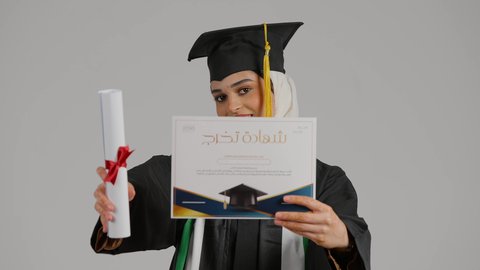 الاحتفالات والمناسبات الجامعية, مفهوم الاجتهاد والتفوق، إنهاء الدراسة الجامعية، الشعور بالفخر والثقة بالنفس، جودة التعليم في المملكة، النظر الى الكاميرا بايماءات السرور، تصوير مقرب لطالبة عربية خليجية اماراتيه محجبة ترتدي عباءه وقبعة التخرج ، تضع وشاح علم الامارات على كتفها، تحمل بيدها وثيقه النجاح