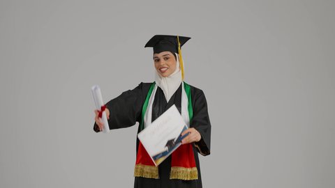 مفهوم الاجتهاد والتفوق، إنهاء الدراسة الجامعية، الشعور بالفخر والثقة بالنفس، جودة التعليم في المملكة، النظر الى الكاميرا بايماءات السرور،الاحتفالات و المناسبات الجامعية, تصوير مقرب لطالبة عربية خليجية اماراتيه محجبة ترتدي عباءه وقبعة التخرج ، تضع وشاح علم الامارات على كتفها، تحمل بيدها وثيقه النجاح