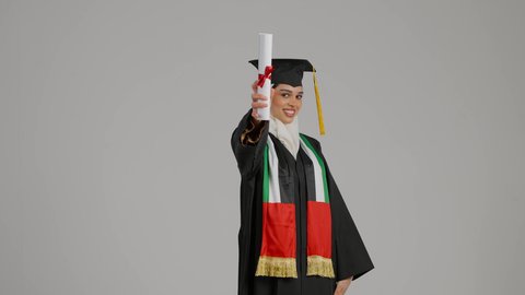 إنهاء الدراسة الجامعية، الشعور بالفخر والثقة بالنفس، جودة التعليم في المملكة، النظر الى الكاميرا بايماءات السرور،الاحتفالات و المناسبات الجامعية, مفهوم الاجتهاد والتفوق، تصوير مقرب لطالبة عربية خليجية اماراتيه محجبة ترتدي عباءه وقبعة التخرج ، تضع وشاح علم الامارات على كتفها، تحمل بيدها وثيقه النجاح