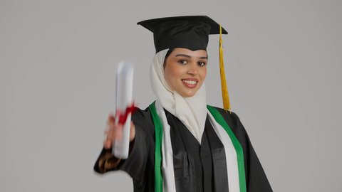 الشعور بالفخر والثقة بالنفس، جودة التعليم في المملكة، النظر الى الكاميرا بايماءات السرور،الاحتفالات و المناسبات الجامعية, إنهاء الدراسة الجامعية، مفهوم الاجتهاد والتفوق، تصوير مقرب لطالبة عربية خليجية اماراتيه محجبة ترتدي عباءه وقبعة التخرج تحمل بيدها وثيقه النجاح