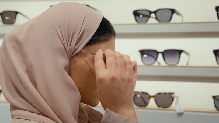 Buying sunglasses, a new wide range of eyeglasses in a Gulf store, a close-up of an Emirati Gulf Arab woman wearing a colorful abaya choosing sunglasses from inside the drawers, a Saudi woman shopping inside the mall