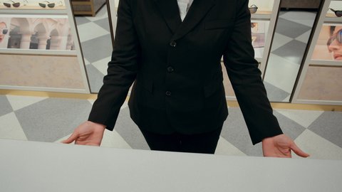 كيفية إختيار النظارة الشمسية الملائمة لملامح الوجه ، اقتناء نظارات حماية من الشمس، تصوير من الامام لبائعه خليجيه تقوم بعرض النظارات الشمسيه الموجوده في الادراج المغقله، تشكيلة واسعة جديدة من نظارات النظر في محل خليجي