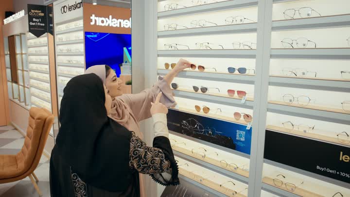 كيفية إختيار النظارة الشمسية الملائمة لملامح الوجه ، اقتناء نظارات حماية من الشمس، امراتان عربيتان خليجيتان اماراتيان ترتديان الحجاب و العباءة تتشاركان لحظه مرحه اثناء فحص اطار نظارة شمسيه،تعابير الإعجاب والرضا، مفهوم القبول والموافقه