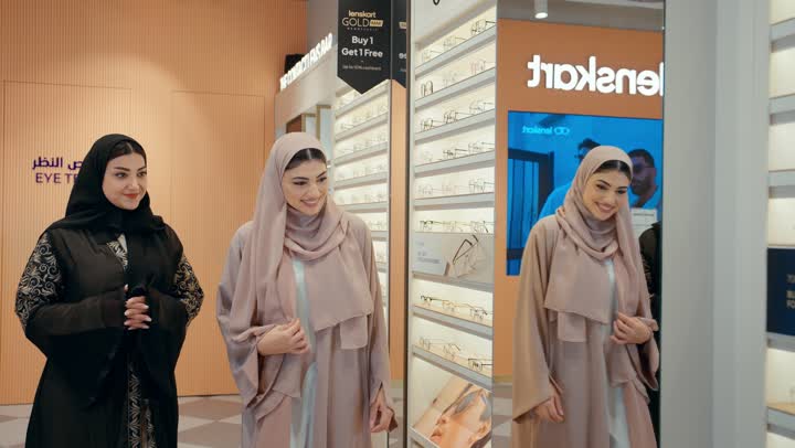 Shopping and choosing glasses inside an optical store, two Emirati Gulf Arab women wearing hijab and abaya share a fun moment while examining eyeglass frames, exchanging opinions and participating in shopping